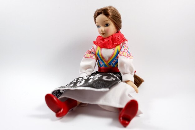 Bella muñeca con un vestido y zapatos rojos Muñeca sentada sobre un fondo blanco