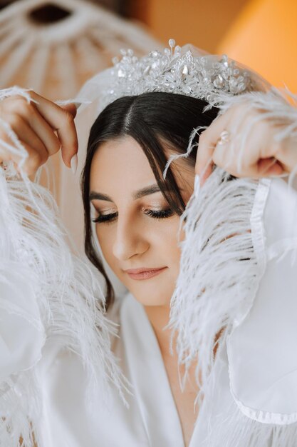 Bella novia en bata la mañana antes de la ceremonia de la boda Increíble peinado de la novia Maquillaje natural y moderno Retrato de una joven novia en bata