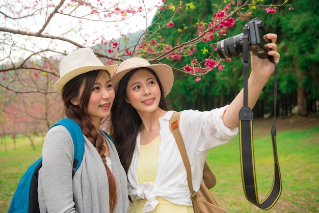 bellas novias usando una cámara profesional tomando selfie fotográfico junto con flores rosas de sakura en la calle de los cerezos en flor en las vacaciones de Japón.