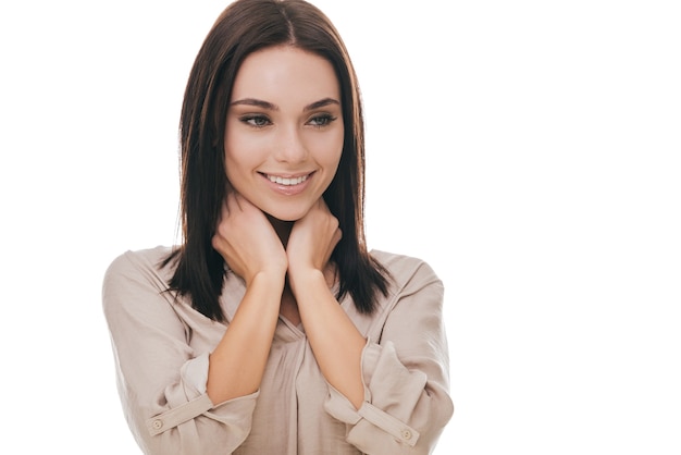 Belleza alegre. Atractiva mujer joven cogidos de la mano en el cuello y sonriendo mientras está de pie contra el fondo blanco.