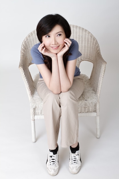 Belleza asiática sentada en una silla con expresión adorable.