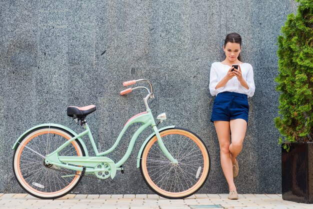 Belleza con bicicleta vintage. Hermosa joven sonriente de pie cerca de su bicicleta vintage en la calle