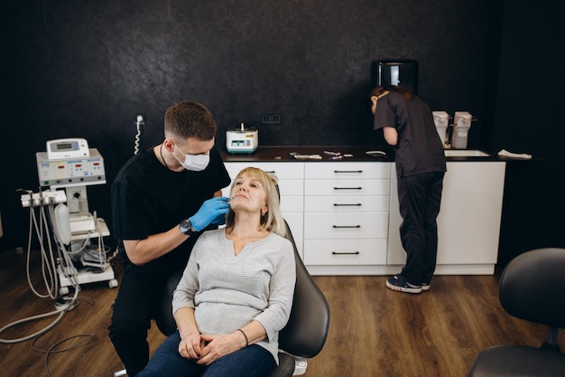 Belleza de Botox y mujer mayor con cirugía plástica en un estudio para el cuidado de la piel y relleno de arrugas Manos de cirujano plástico y cara de mujer mayor para levantamiento de colágeno e inyección de silicona