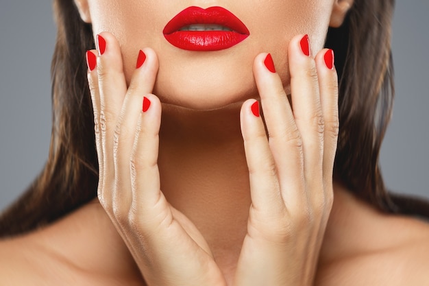 Foto belleza y cosmética. boca femenina y uñas con manicura roja y lápiz labial.