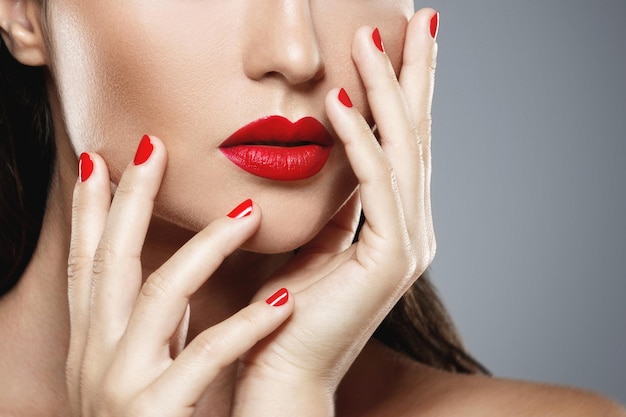 Belleza y cosmética. Primer plano de la boca femenina y las uñas con manicura roja y lápiz labial.