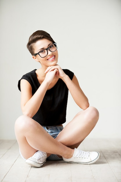 Belleza con estilo. Retrato de mujer joven hermosa de pelo corto sentada en el suelo y sonriendo