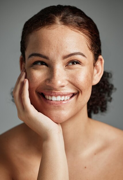 Foto belleza facial y cuidado de la piel de una mujer en un estudio aislado en un fondo gris pensando en cosméticos de maquillaje y feliz modelo femenino satisfecho con un tratamiento facial de spa para una piel brillante y saludable o impecable