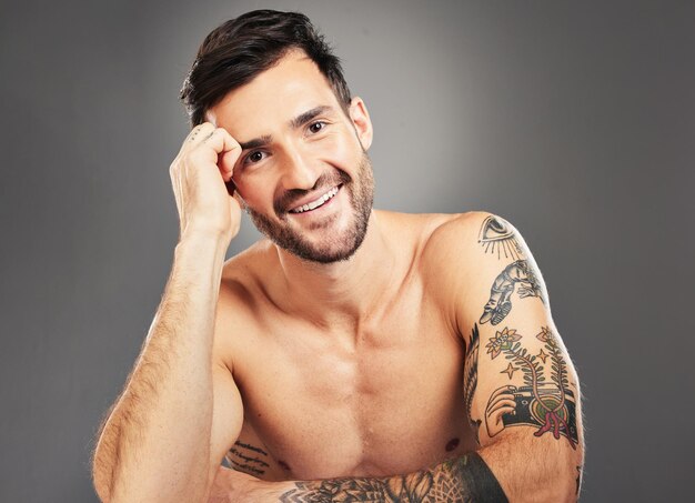 Belleza de hombre y sexy con tatuaje corporal y retrato feliz sobre fondo gris de estudio con espacio de maqueta Modelo masculino sexy y sonrisa para cuidado de la piel y bienestar cosmético con cara limpia