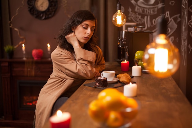 Belleza joven morena sentada en el bar con una taza de café y un sabroso pastel en una cafetería de lujo. Retrato de mujer joven pensativamente.