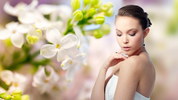 belleza, joyería, gente y concepto de lujo - hermosa mujer asiática o novia con arete y anillo de dedo sobre fondo de flor de lila de manantial natural