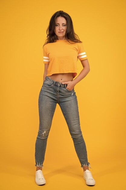 Foto belleza y maquillaje chica bonita con cabello largo moda y estilo los vaqueros delgados le van bien la confianza en sí misma es el mejor traje chica sexy de fondo amarillo chica sexy chica sensual en estilo casual