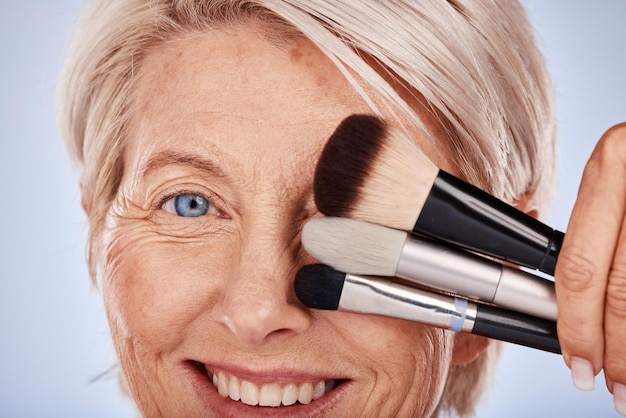 Belleza de maquillaje y mujer mayor con cepillo para la elección de productos para el cuidado de la piel facial y promoción de la base en el estudio