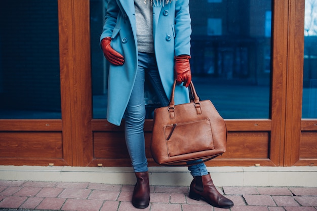 Belleza y moda. Elegante mujer de moda con abrigo y guantes, sosteniendo el bolso bolso marrón