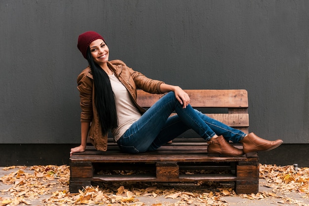 Belleza de moda. Hermosa joven sentada en la plataforma de madera y sonriendo