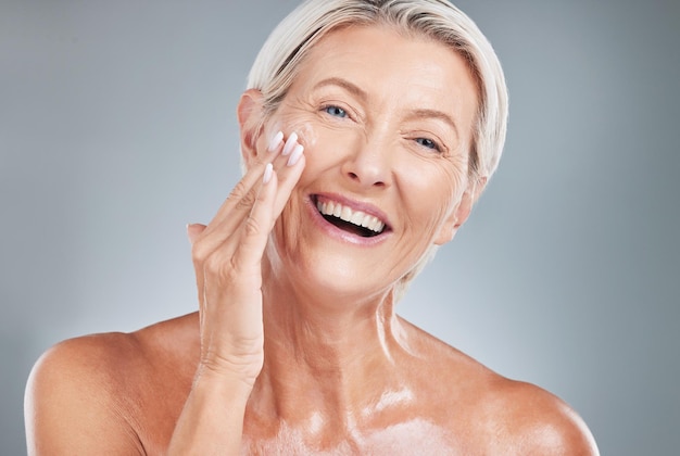 Belleza de mujer mayor y sonrisa para crema hidratante para el cuidado de la piel o tratamiento cosmético contra un fondo gris de estudio Mujer anciana feliz sonriendo con dientes en satisfacción por una crema facial perfecta para la piel