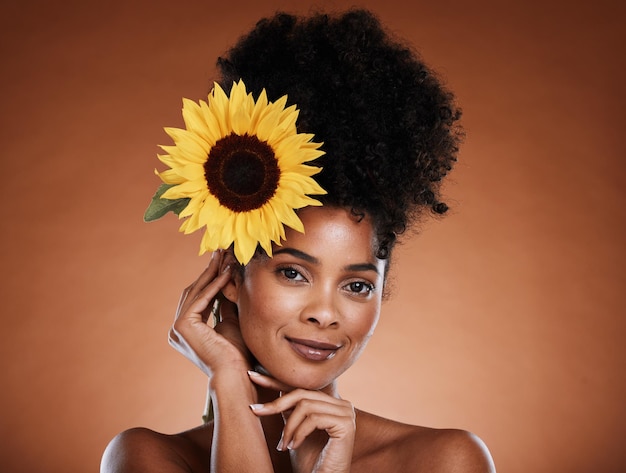 Belleza de mujer negra y flor para cosméticos orgánicos para la salud estética y el bienestar en un fondo de estudio marrón Girasol de maquillaje y mujer afroamericana con la cara limpia para el cuidado de la piel
