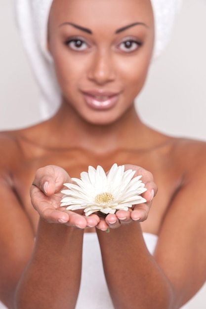 Belleza natural. Hermosa joven sin camisa afroamericana sosteniendo una flor en sus manos y mirando a la cámara mientras está aislado sobre fondo gris