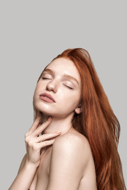 Belleza natural joven y tierna mujer pelirroja tocando su piel suave y manteniendo los ojos cerrados