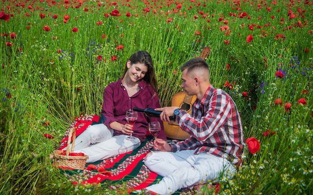 Belleza de la naturaleza de primavera. amor y romance. relación romántica. pareja enamorada de la guitarra beber vino. hombre y mujer en campo de flores de amapola. vacaciones de verano. familia feliz. la música country. Siempre tuyo.