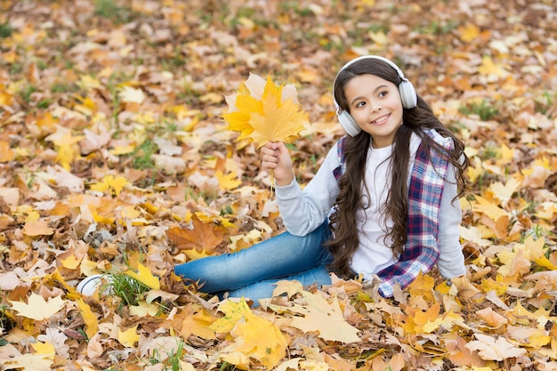 Belleza pensativa. moda infantil de otoño. inspiración. infancia feliz. De vuelta a la escuela. chica entre hojas de arce relajarse en el parque. caer en el bosque. disfruta de la música en los auriculares. educación en línea y e-learning.