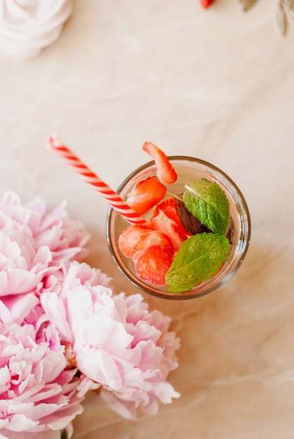 Belleza plana, con agua de desintoxicación de fresa, accesorios y peonías sobre un fondo de mármol.