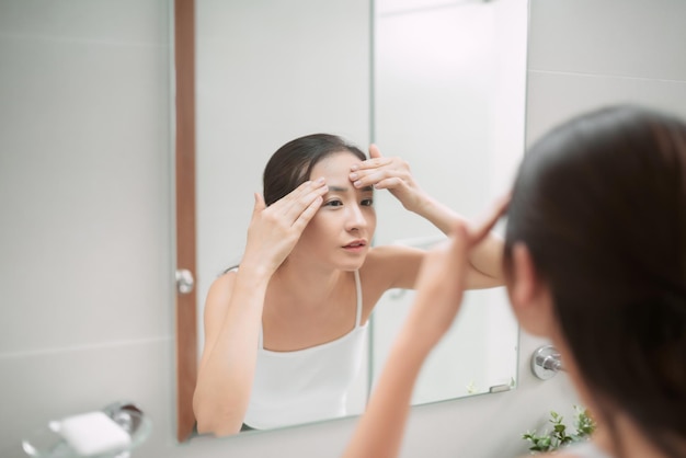 Belleza en el reflejo del espejo Vista sobre el hombro de una mujer hermosa tocándose la cara mientras se mira en el espejo
