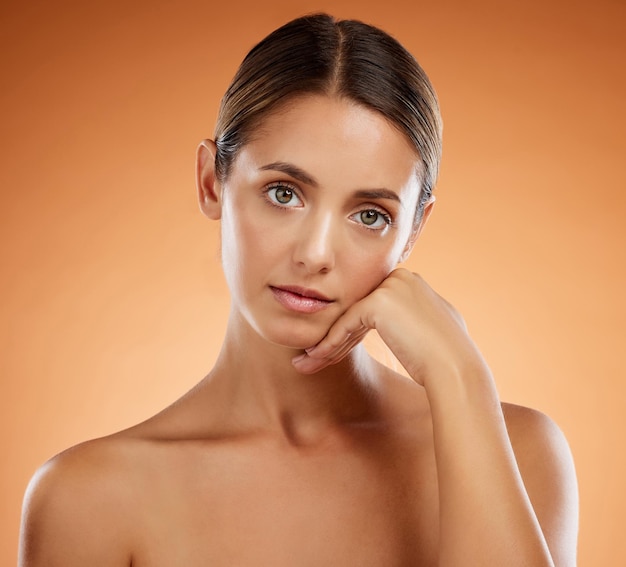 Belleza y retrato para el cuidado de la piel con pose de mano y rostro serio de mujer hermosa con cuerpo resplandeciente Chica modelo de fondo naranja con sensación natural joven y cosmética en la piel en el estudio