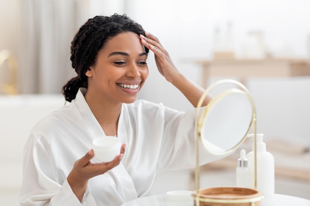 Belleza rutina atractiva mujer negra aplicando crema hidratante en la cara