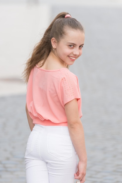 Belleza sonriente. Chica de belleza feliz en el día de verano. Mirada de belleza de adorable niña pequeña en el fondo urbano. Niño pequeño con una sonrisa encantadora en la cara de la belleza y el cabello largo y hermoso.