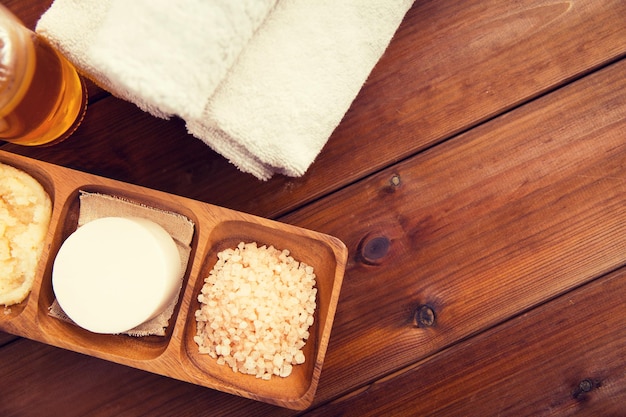 belleza, spa, cuidado del cuerpo, cosmética natural y concepto de bienestar - cierre de soa con sal rosa del himalaya y toallas de baño sobre una mesa de madera