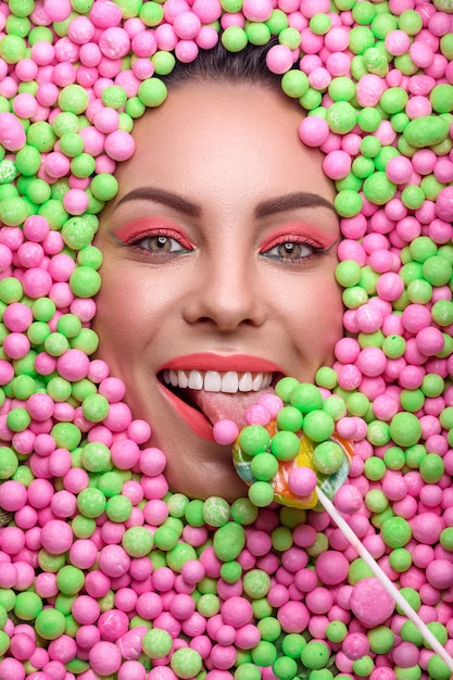 Bello rostro de una mujer joven con maquillaje creativo rodeado de varios dulces