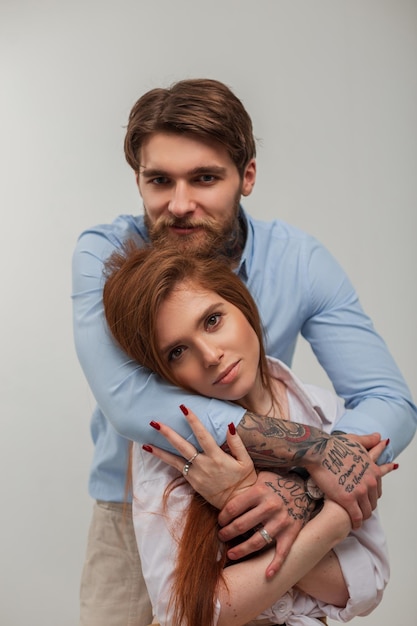 Belo casal jovem elegante em elegantes roupas casuais elegantes no estúdio Bela jovem ruiva feliz e bonito homem moderno moderno com tatuagem e abraço de barba