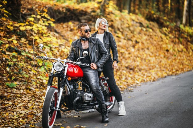 Belo casal perto de moto vermelha na estrada na floresta