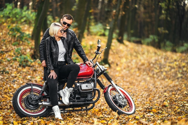 Belo casal perto de moto vermelha na estrada na floresta