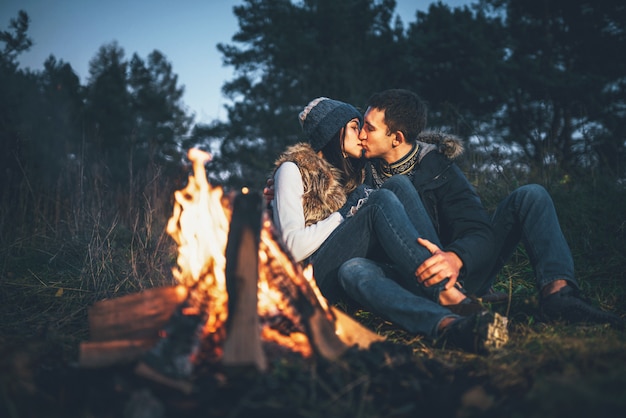 Belo casal relaxante perto da fogueira na floresta no entardecer