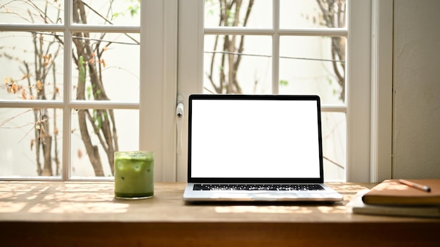 Belo espaço de trabalho mínimo com maquete de laptop e um copo de chá verde gelado em uma mesa de madeira