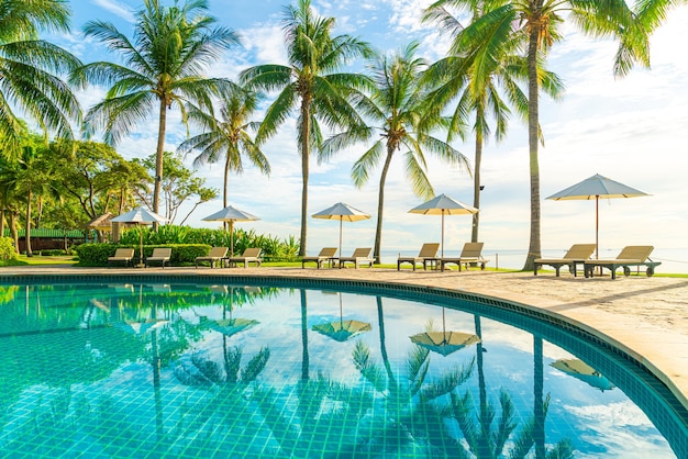 Belo guarda-chuva de luxo e cadeira ao redor da piscina externa do hotel e resort com coqueiro no céu do pôr do sol ou do nascer do sol - conceito de férias e férias