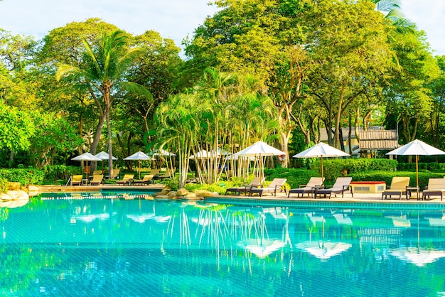 Belo guarda-sol de luxo e cadeira ao redor da piscina externa em hotel e resort com coqueiro