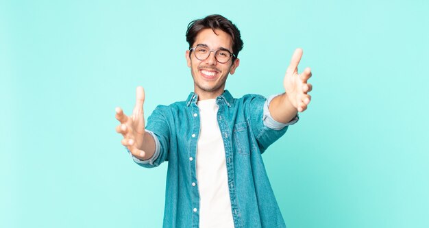 Belo homem hispânico sorrindo alegremente dando um abraço caloroso, amigável e afetuoso de boas-vindas, sentindo-se feliz e adorável