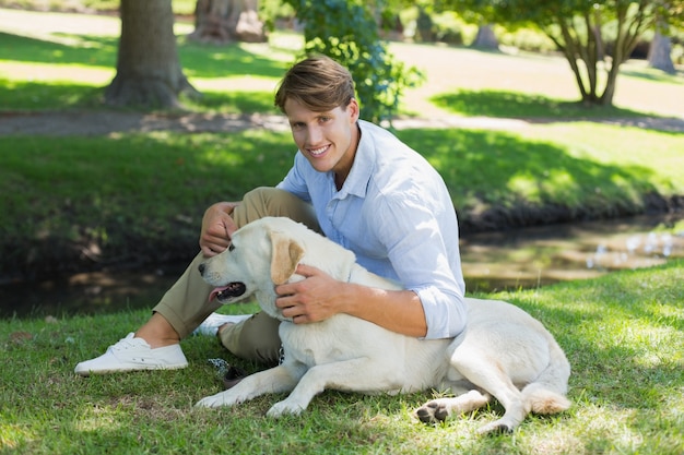 Belo homem sorridente com seu labrador no parque