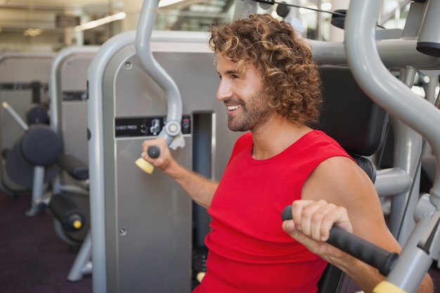 Belo homem sorridente que trabalha na máquina de ginástica na academia