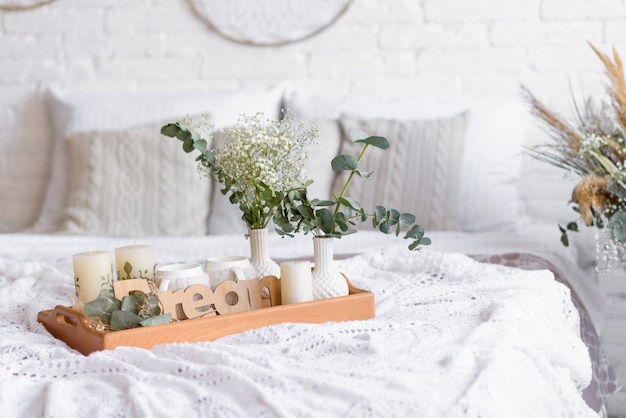 Belo interior em casa com tons de branco e bege, com coletores de sonhos, flores secas e uma cama. Interior de uma casa aconchegante