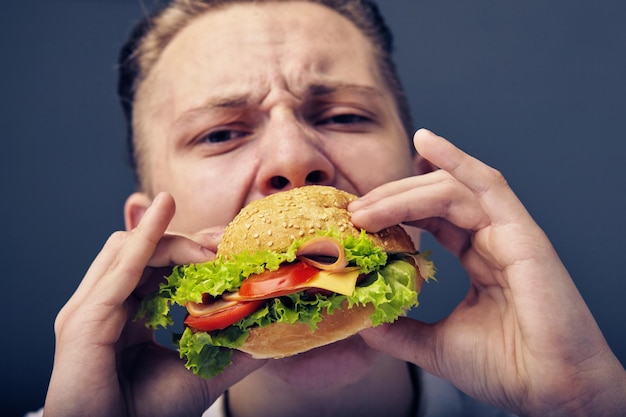 Belo jovem comendo um hambúrguer fresco