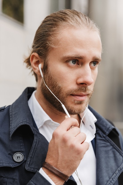 belo jovem empresário confiante usando fones de ouvido, andando nas ruas da cidade