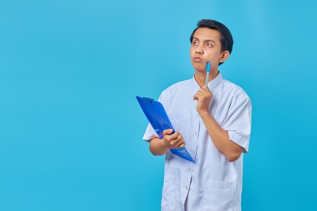 Belo jovem enfermeiro concentrado pensando em ideias sobre um fundo azul