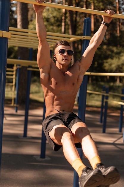 Belo jovem esportivo com corpo musculoso faz exercícios na barra horizontal no parque Esporte e estilo de vida saudável