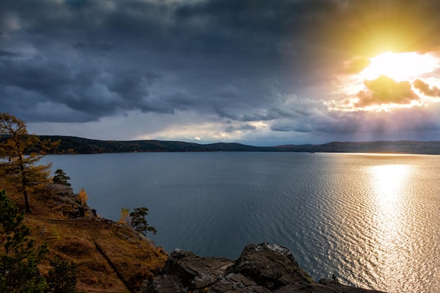 Belo lago e costa rochosa sob os raios do sol da tarde do outono dourado em tempo nublado