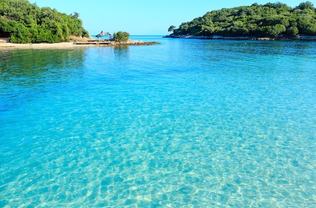 Belo mar Jônico com água turquesa clara e vista da costa de verão de manhã da praia (Ksamil, Albânia). Através de uma água límpida e transparente pode-se ver um bando de pequenos peixes.