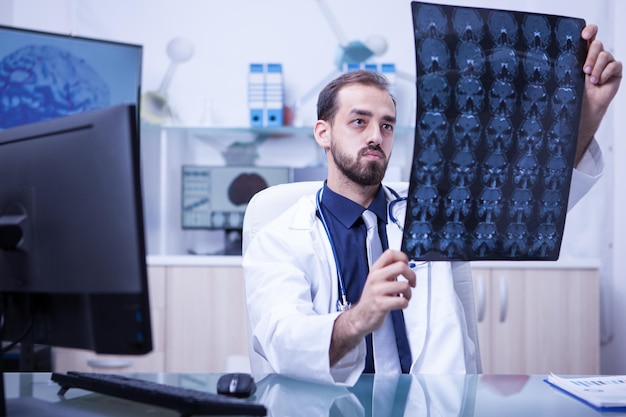 Belo médico neurológico olhando para uma tomografia computadorizada do cérebro no gabinete. Braing imaginando examinado pelo jovem médico.