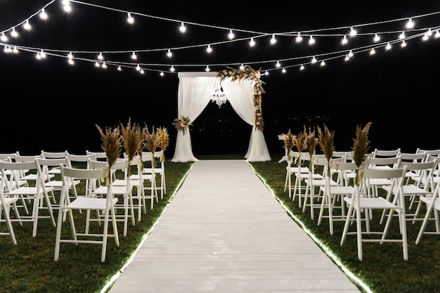 Belo palco noturno para a cerimônia de casamento. arco de madeira de casamento. decoração de casamento elegante. cadeiras para a cerimônia de casamento. lâmpadas decorativas iluminam o local. local de casamento vazio